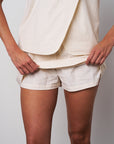 Person wearing a cream-colored blazer and shorts against a plain background