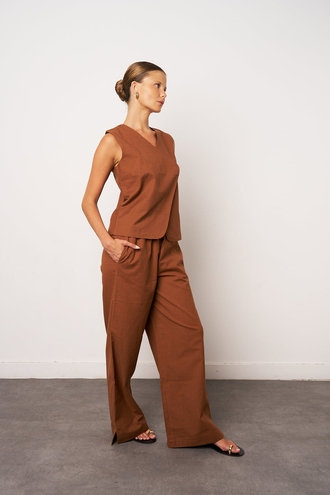 Woman wearing a brown sleeveless top and wide-leg pants against a white wall.
