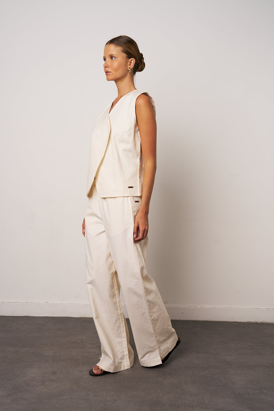 Woman wearing a white sleeveless top and pants against a plain background