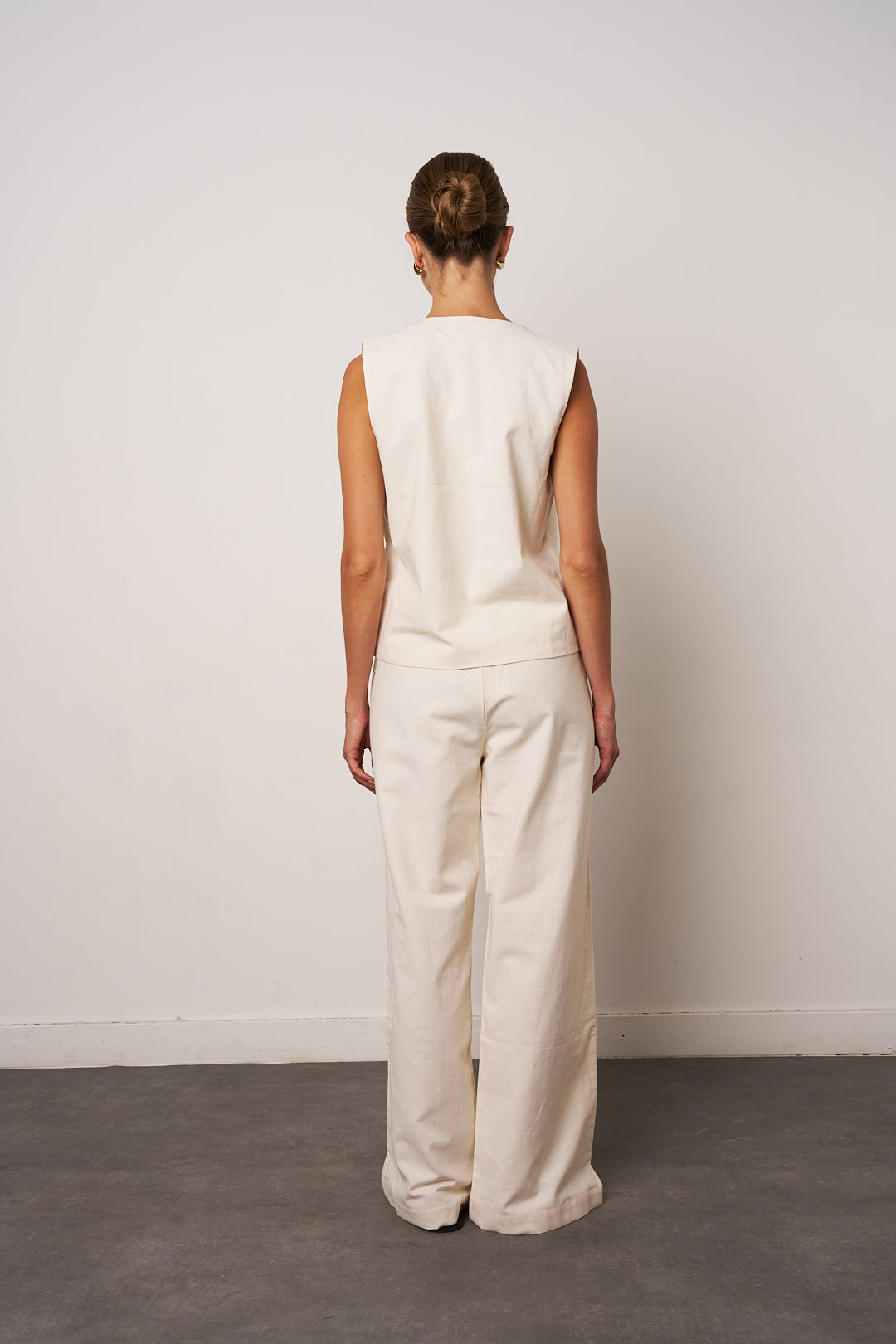 Person wearing a white sleeveless top and pants against a plain background