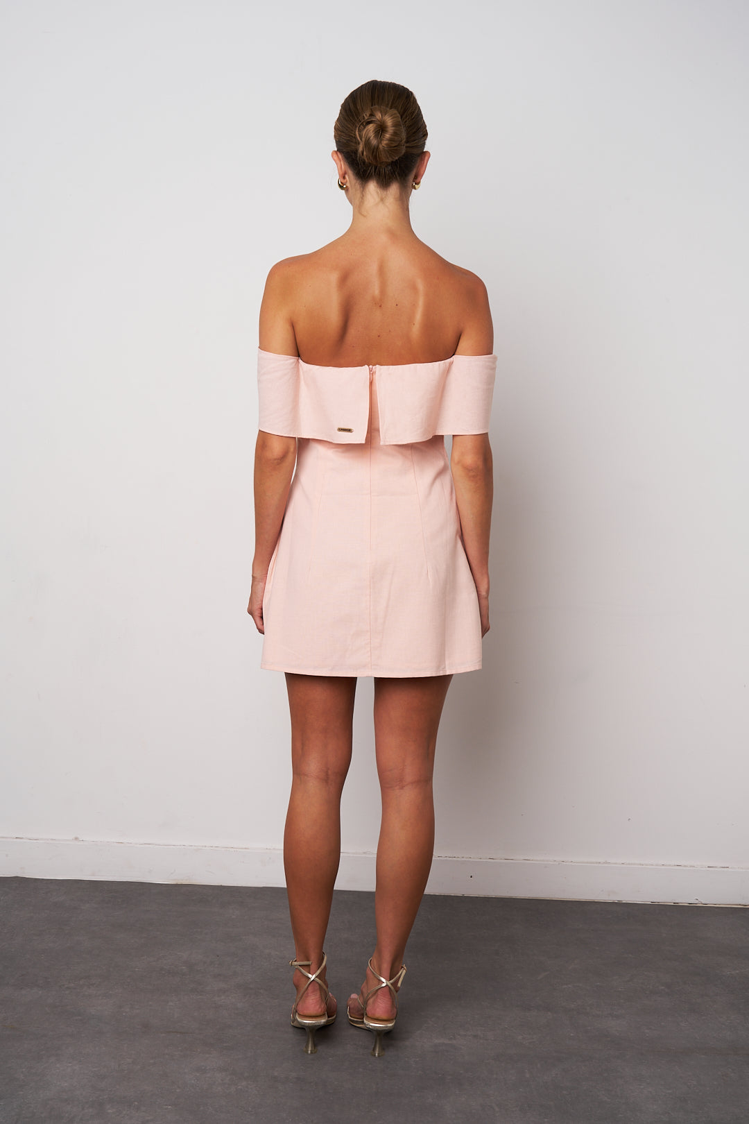Woman wearing a light pink off-shoulder dress against a white background