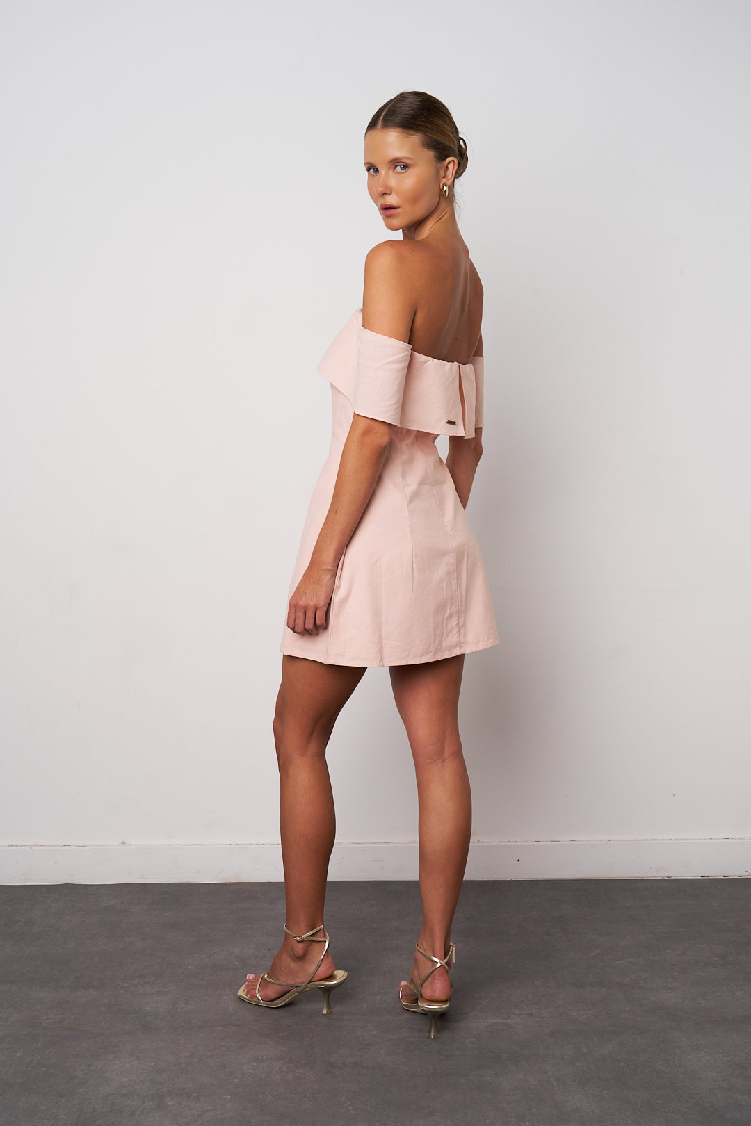 Woman wearing a light pink off-shoulder dress against a white background