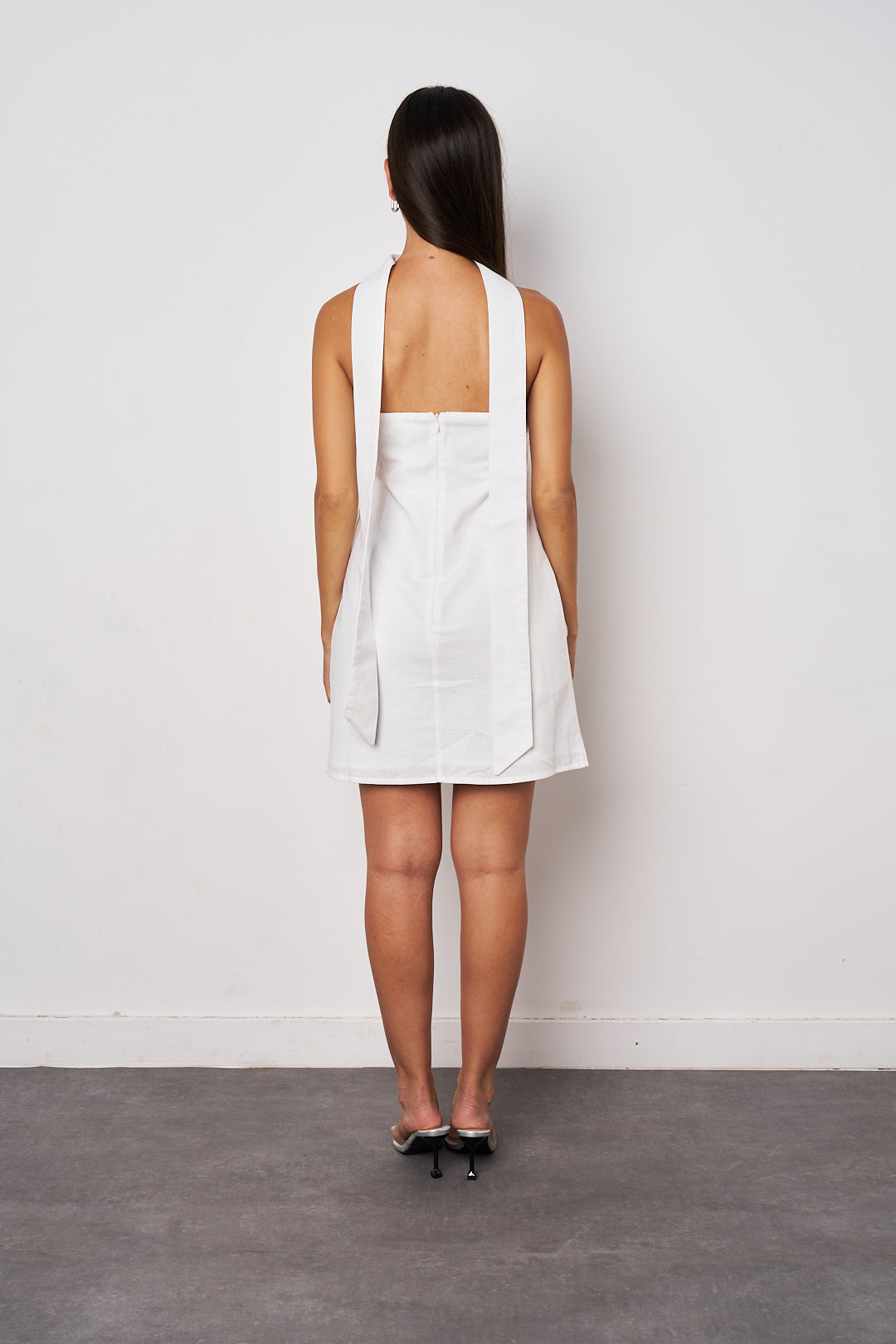 Woman wearing a white dress with a backless design against a plain background