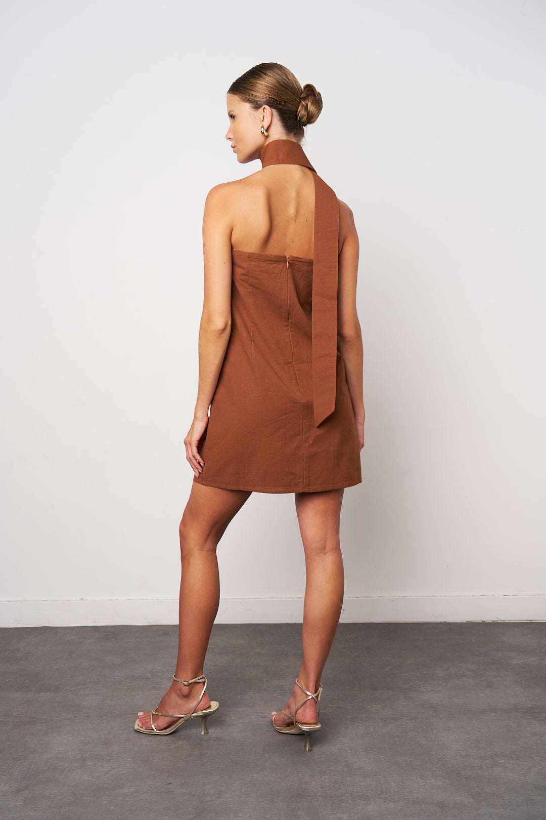 Woman wearing a brown dress with a backless design on a plain background
