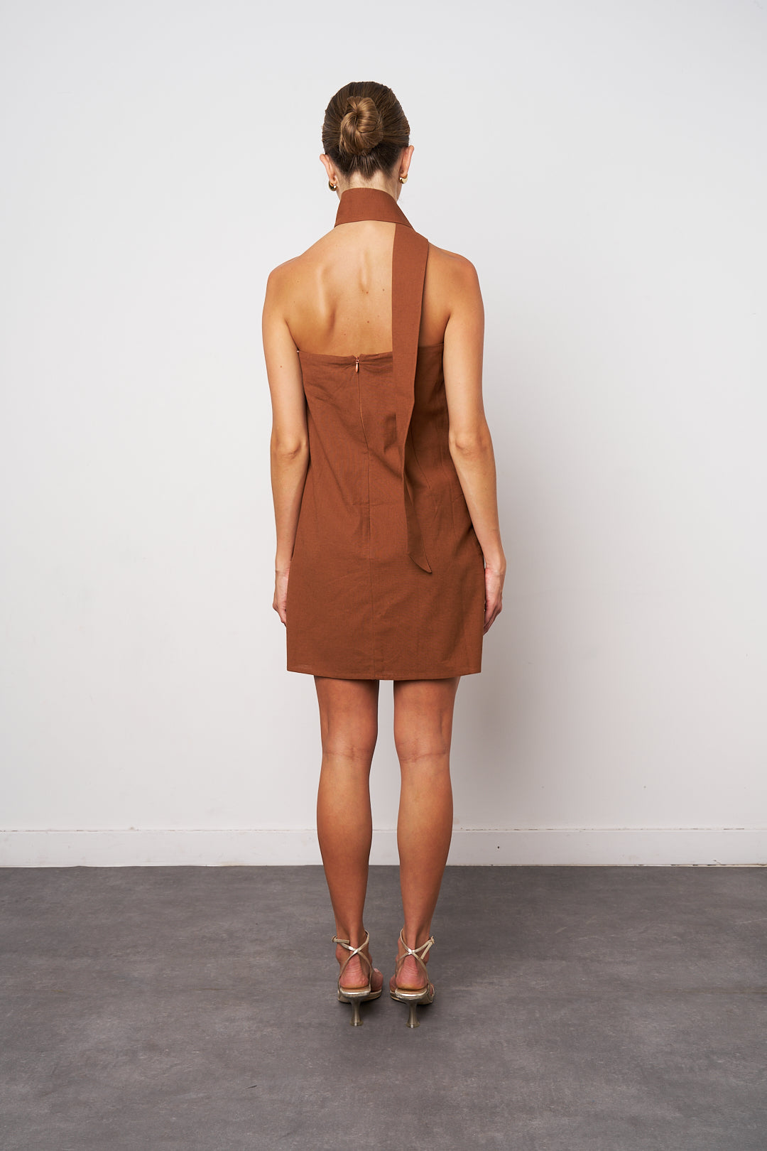 Woman wearing a brown dress with a halter neck design against a white background