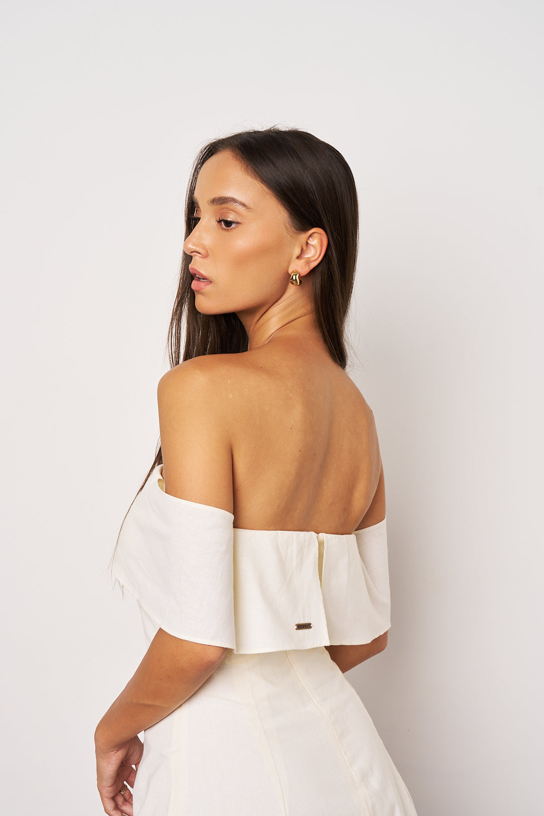Woman wearing a white off-shoulder top against a plain background