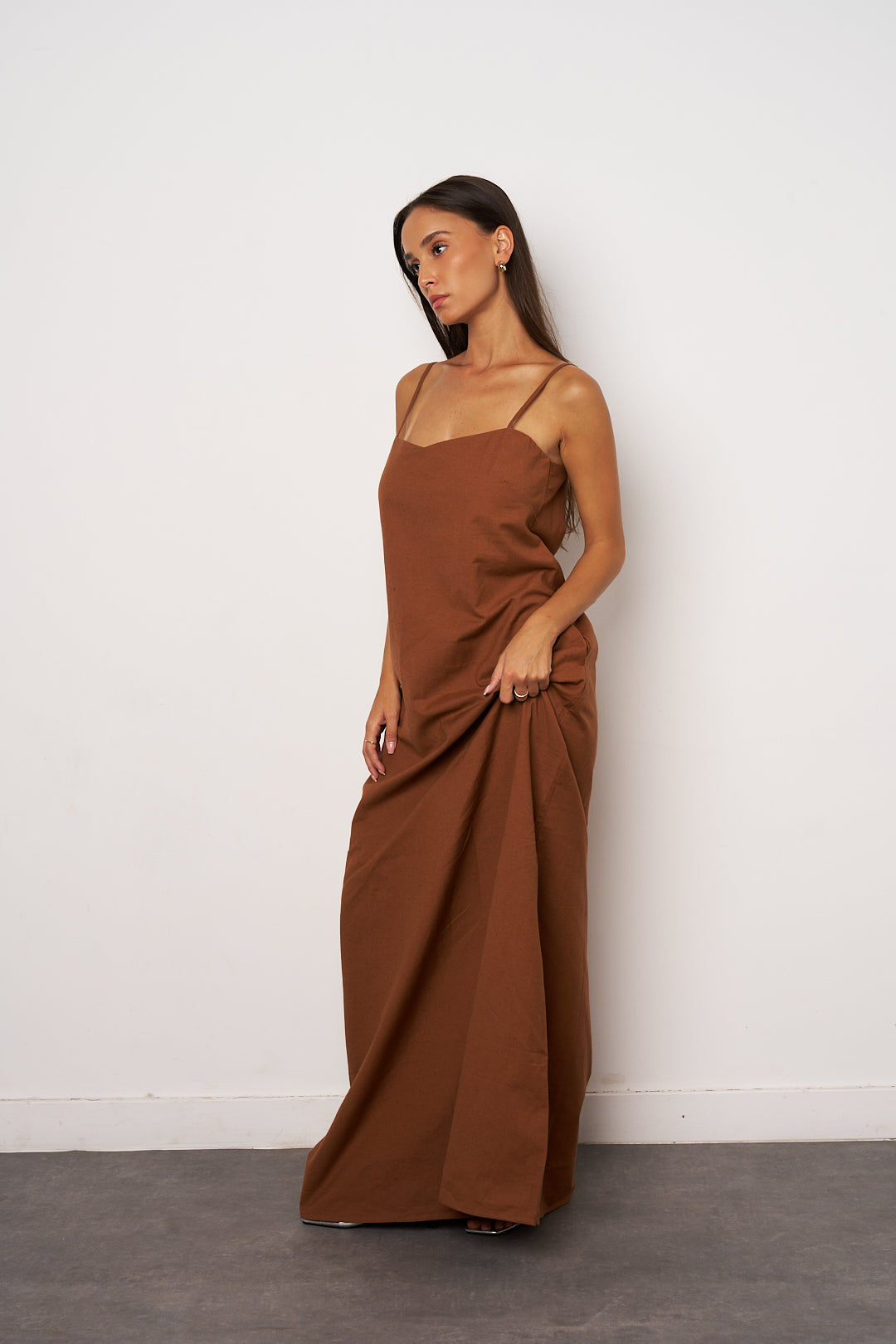Woman wearing a brown maxi dress against a white wall