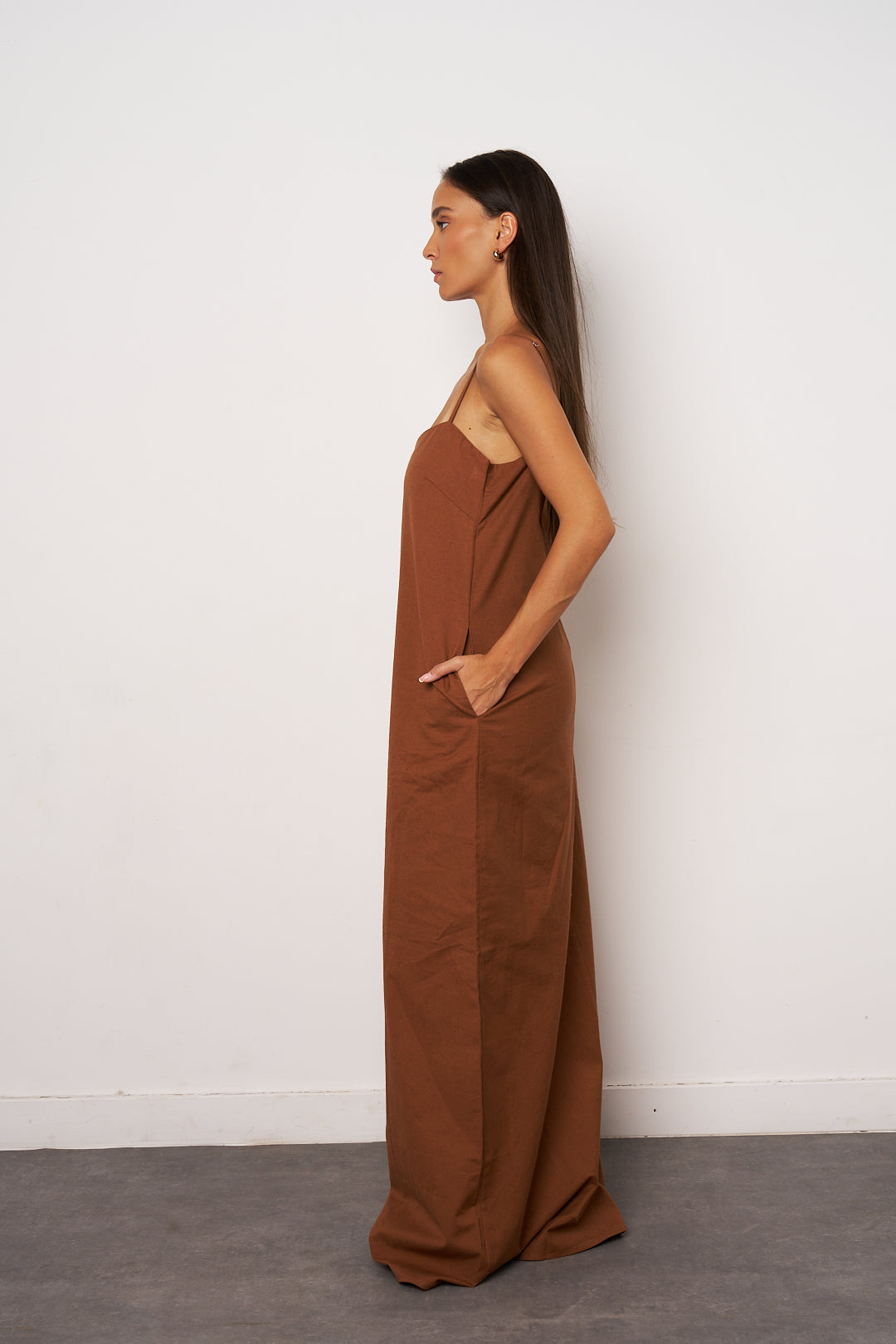 Woman wearing a brown dress against a white wall profile look