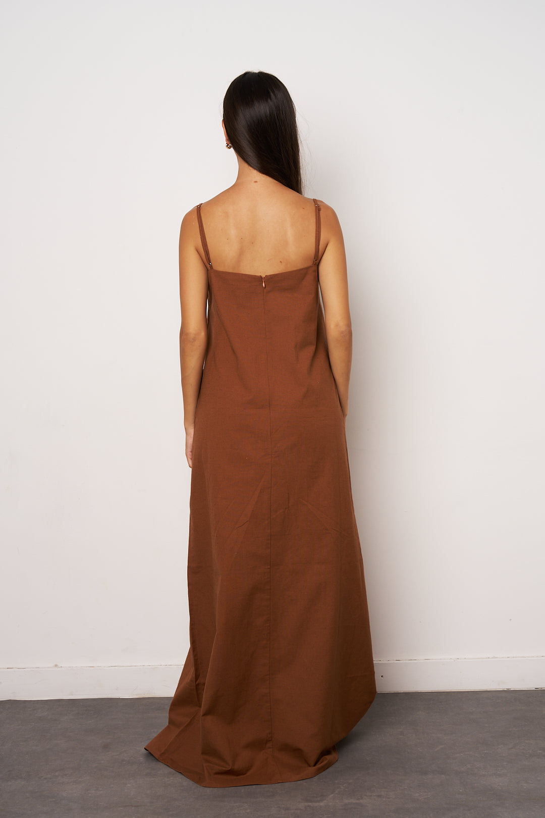 Woman wearing a brown maxi dress against a white background back look