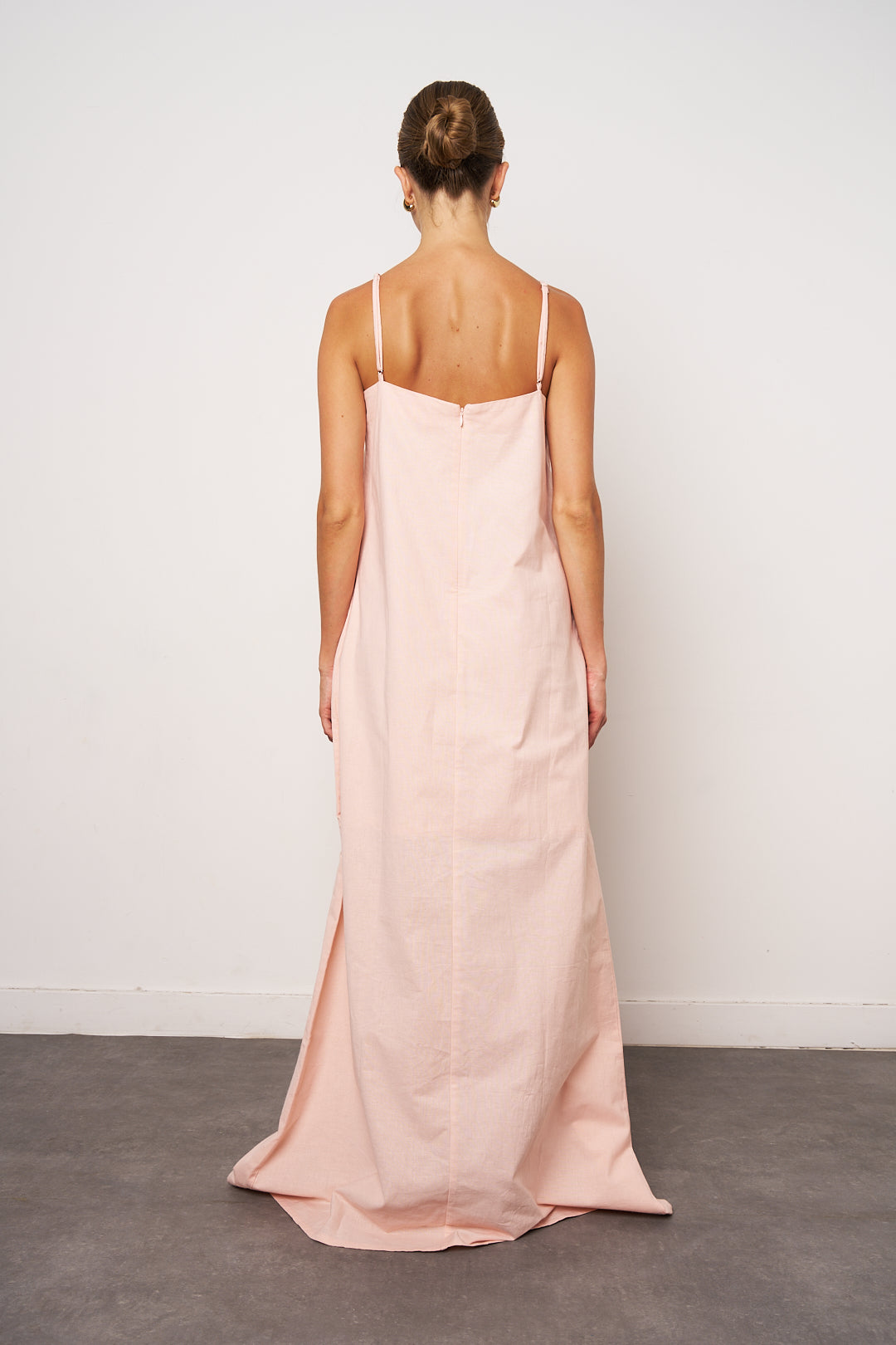 Woman wearing a long pink dress with thin straps against a white background