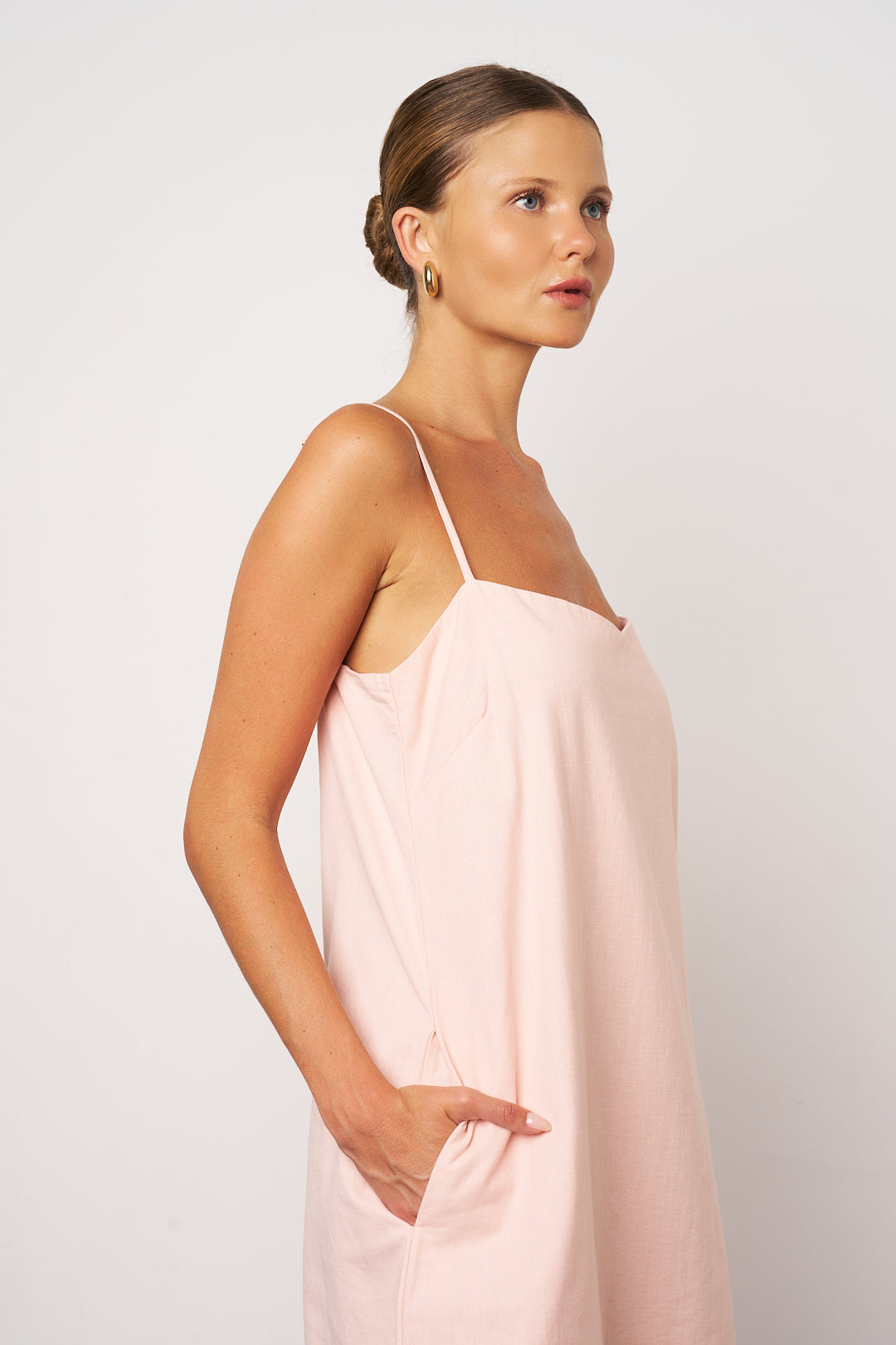 Woman wearing a light pink slip dress against a plain background