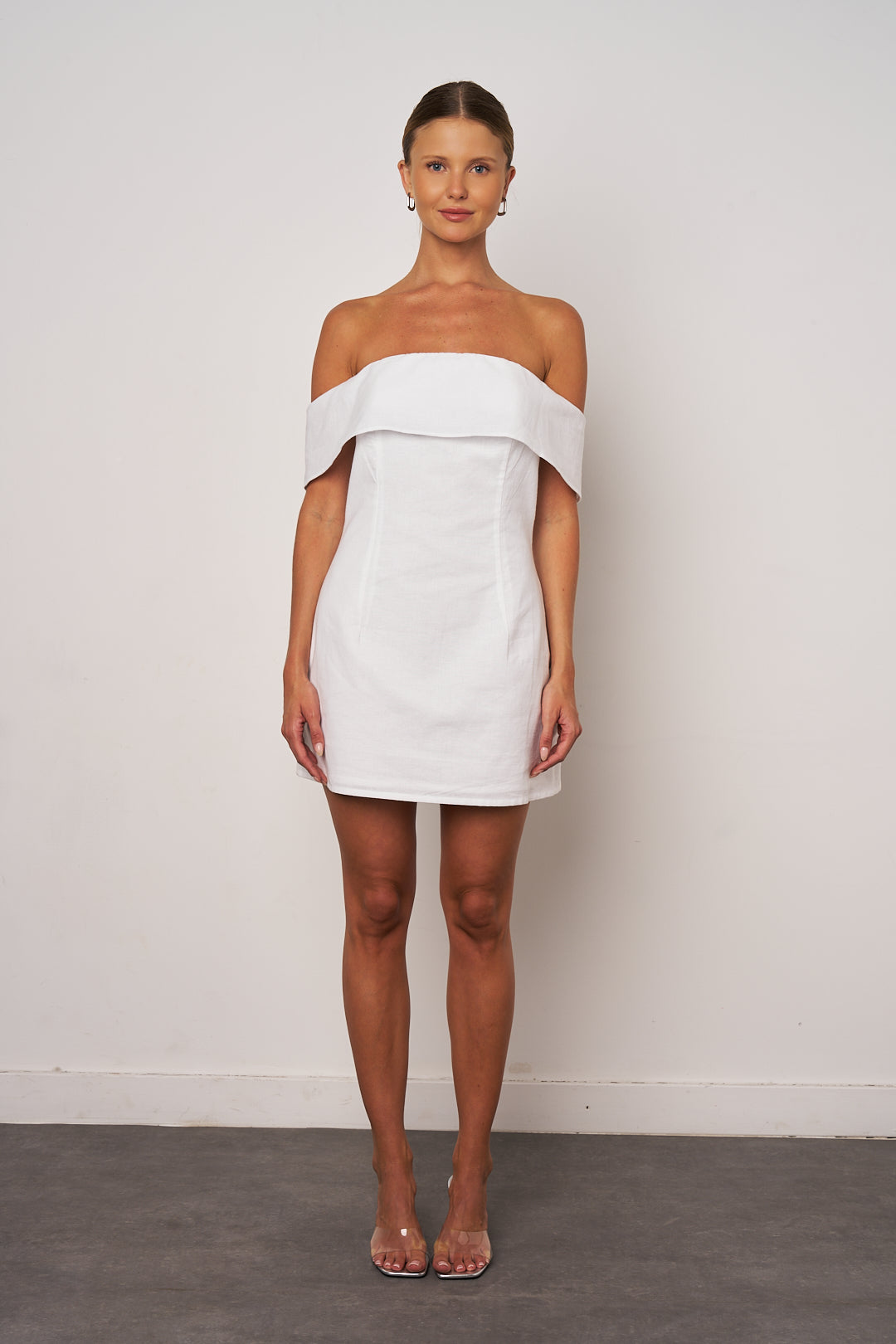Woman wearing a white off-shoulder dress against a plain background