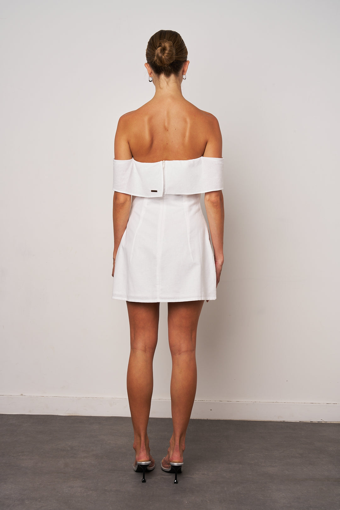 Woman wearing a white off-shoulder dress against a plain background