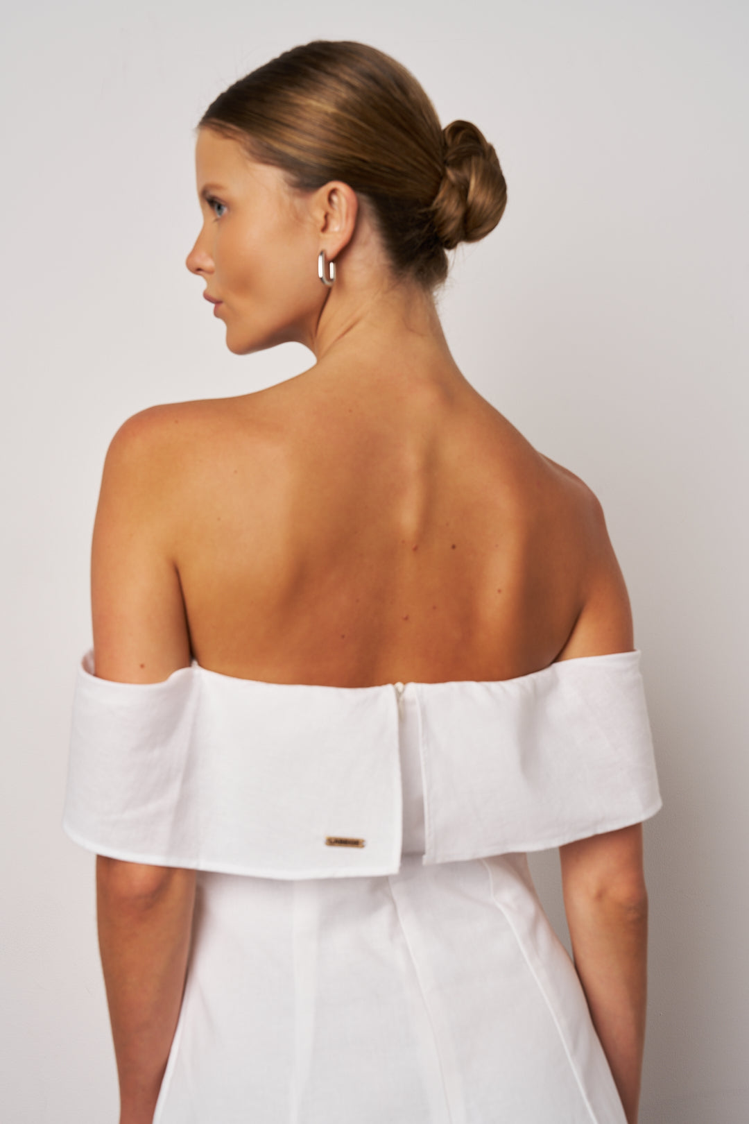 Woman wearing a white off-shoulder dress against a plain background