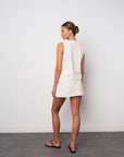 Woman wearing a white sleeveless top and shorts against a plain white wall.