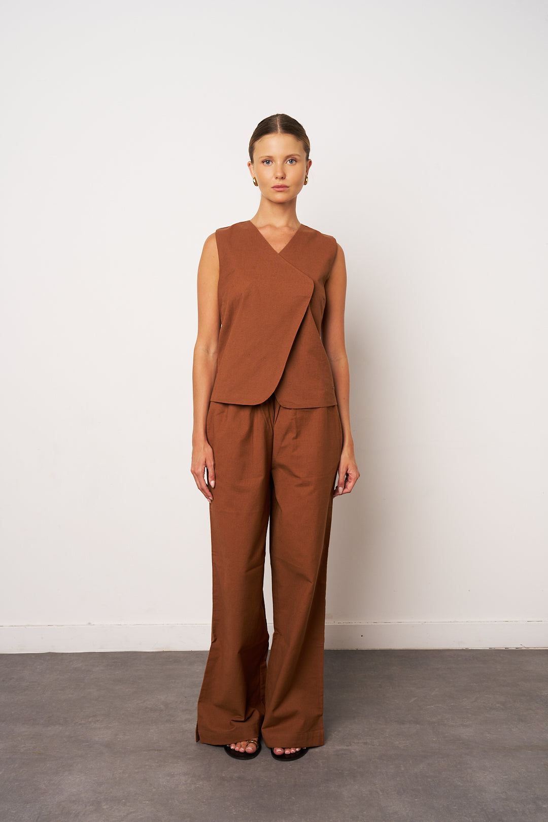 Woman wearing a brown sleeveless top and pants against a white background