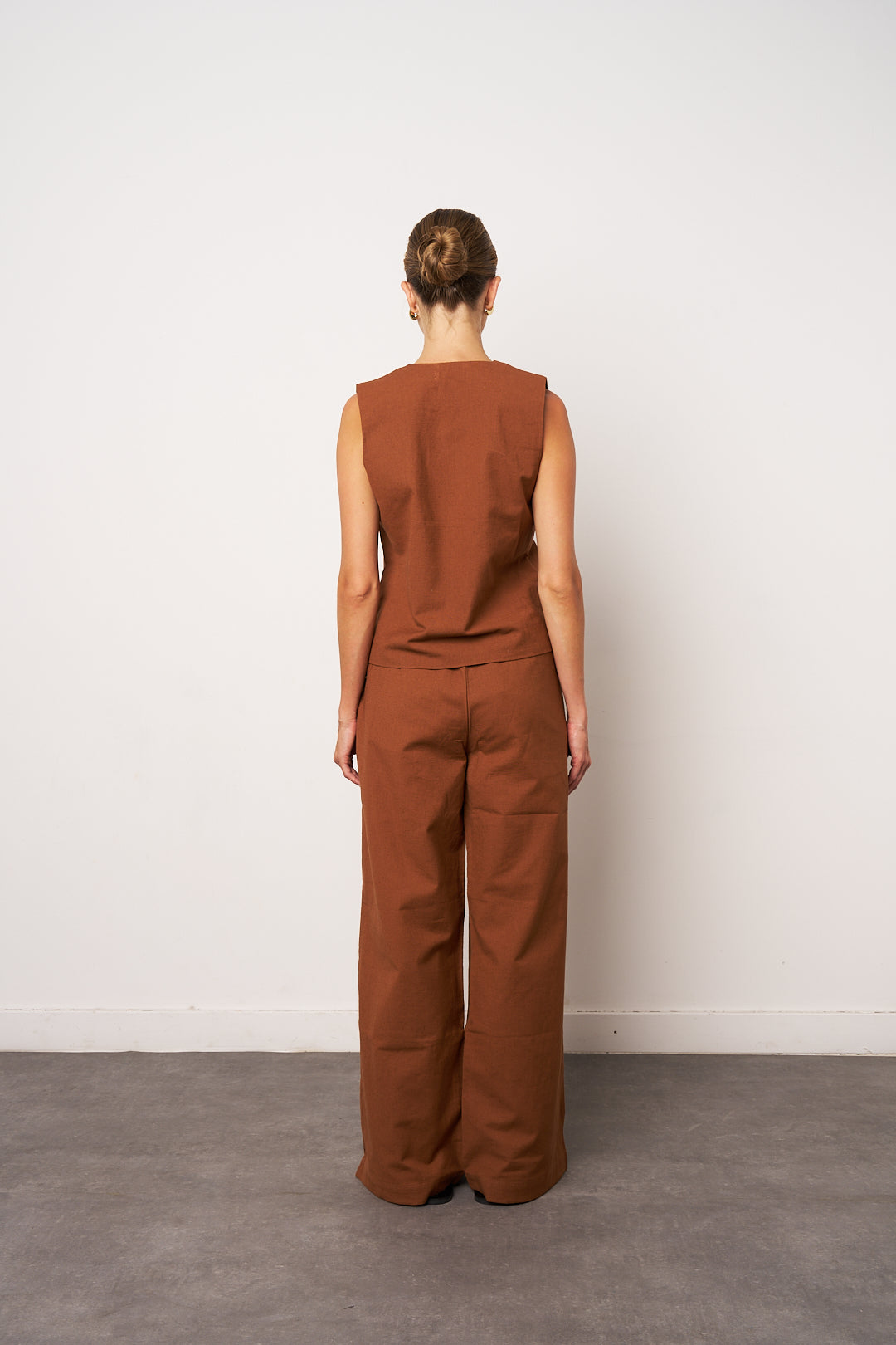 Person wearing a brown sleeveless top and pants against a white wall.