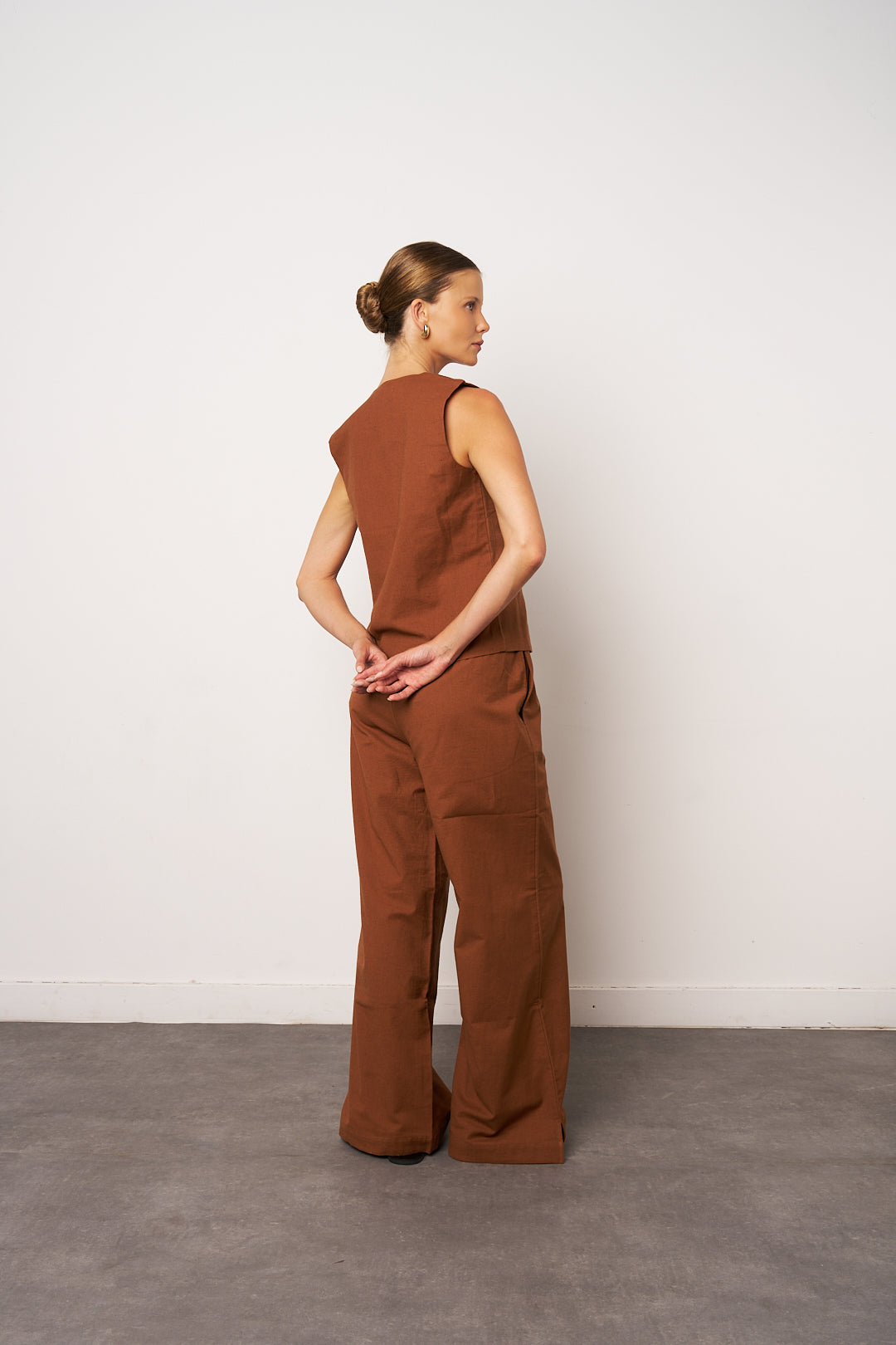 Woman wearing a brown jumpsuit standing against a white wall.