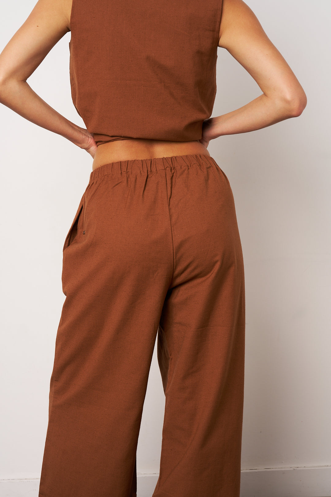 Person wearing a brown sleeveless top and wide-leg pants against a white background