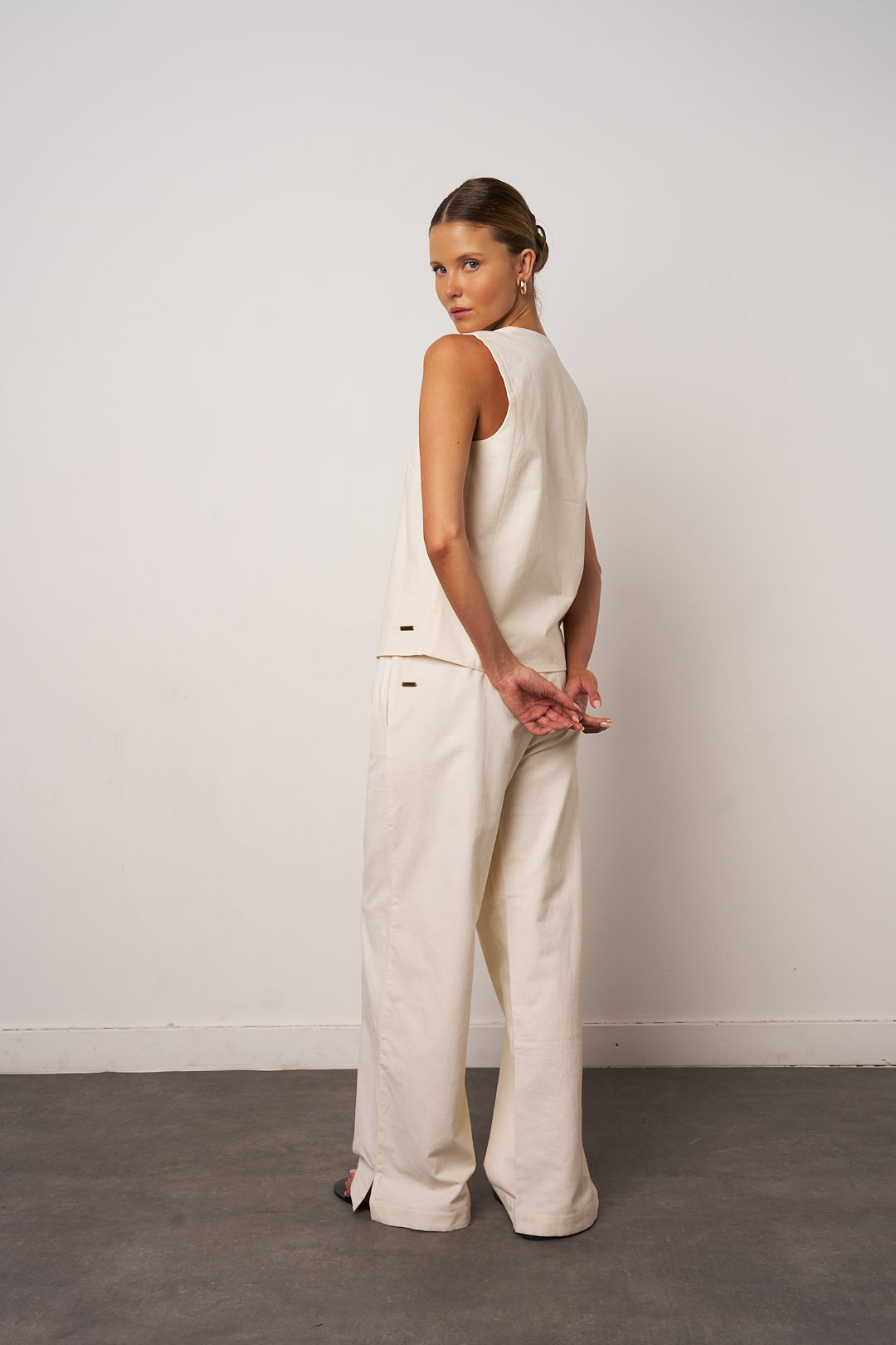 Woman wearing a white sleeveless top and wide-leg pants against a plain background