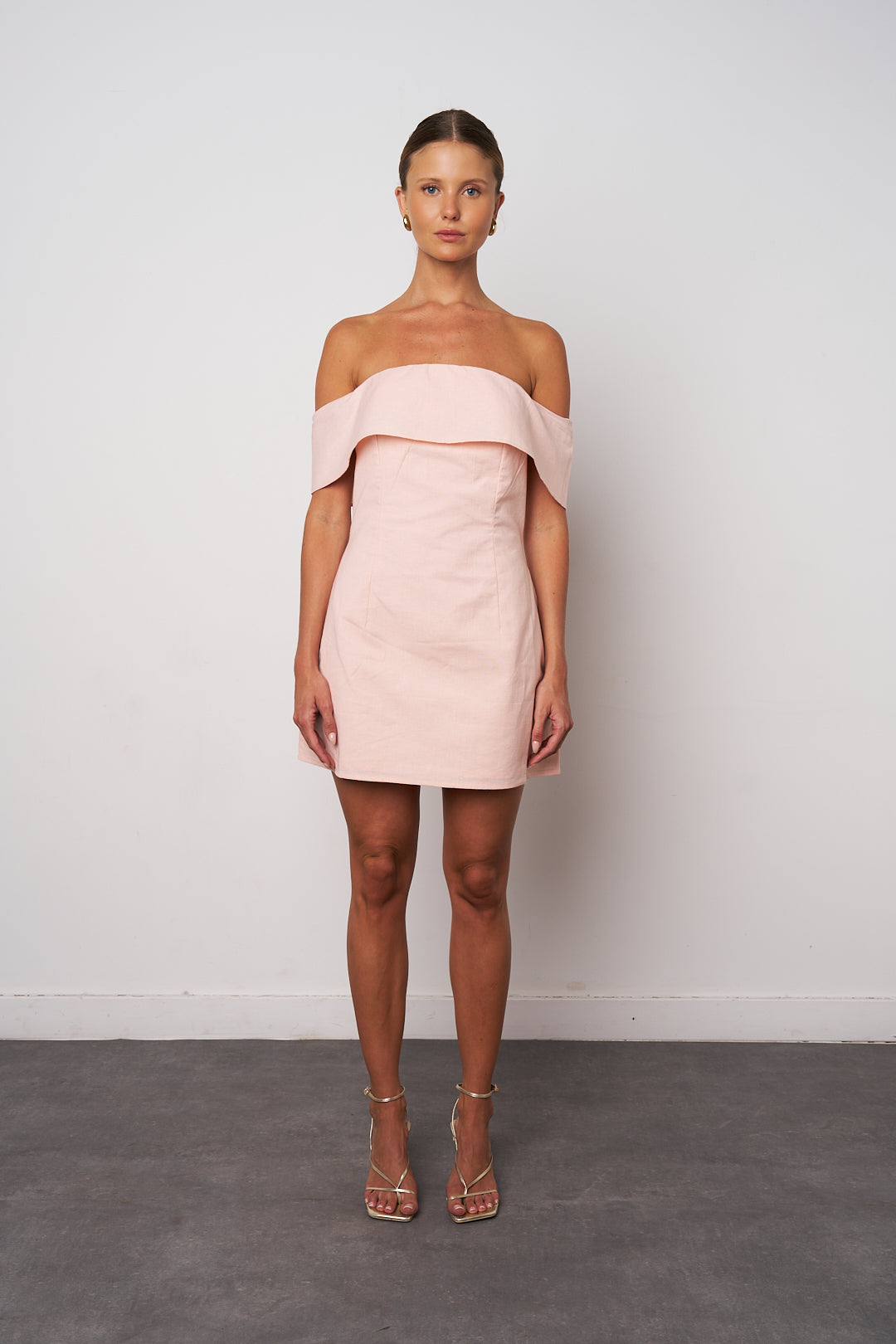 Model wearing a light pink off-shoulder dress against a plain background