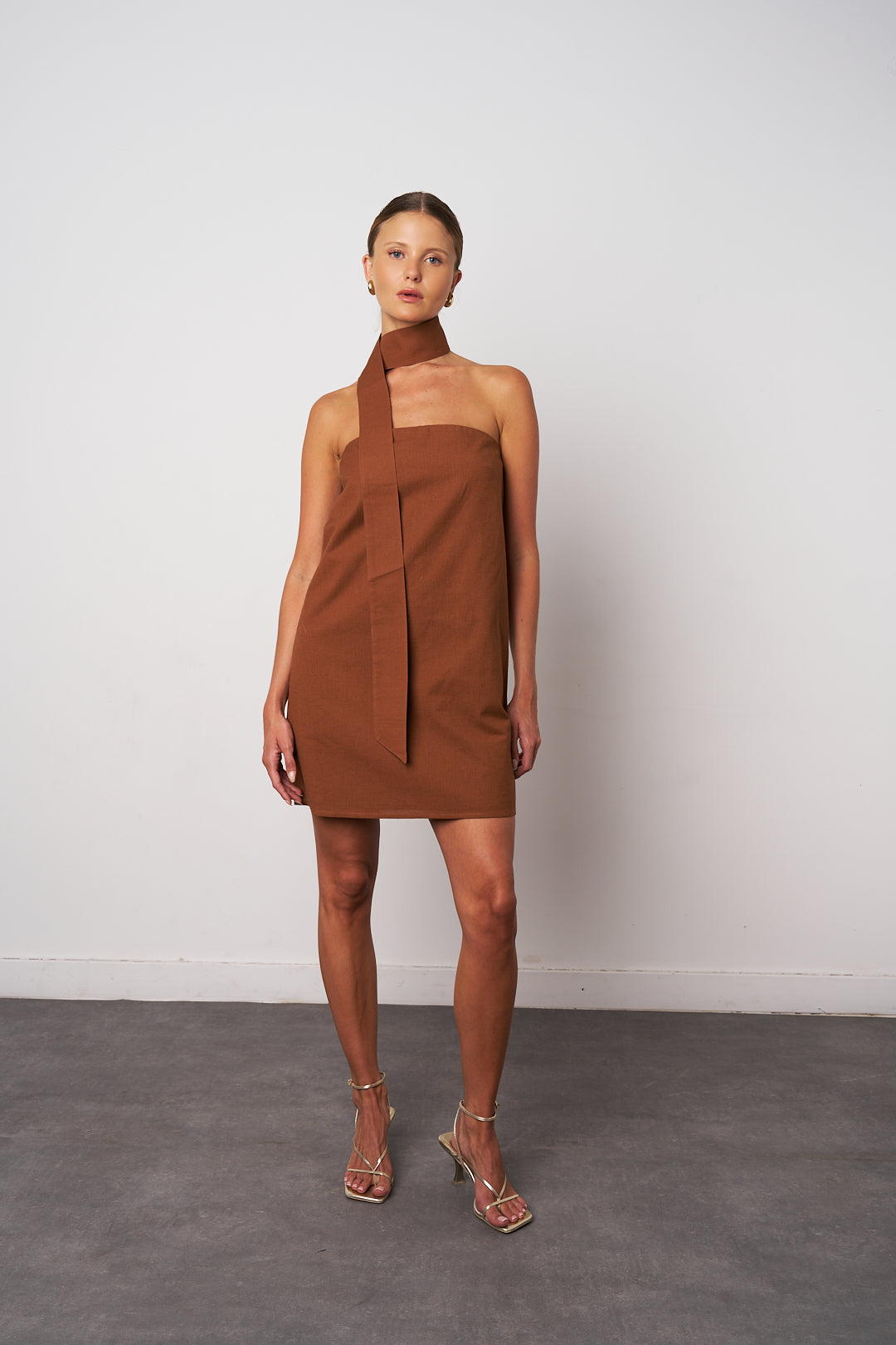 Woman wearing a brown halter neck dress against a white background