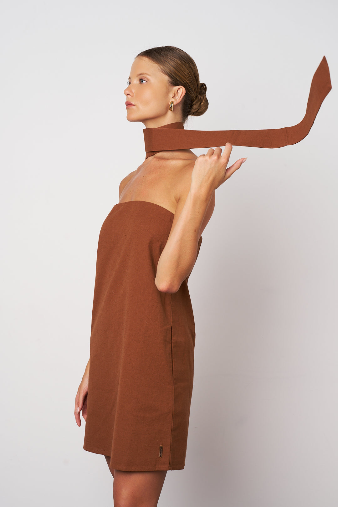 Woman wearing a brown dress holding a long brown belt against a white background