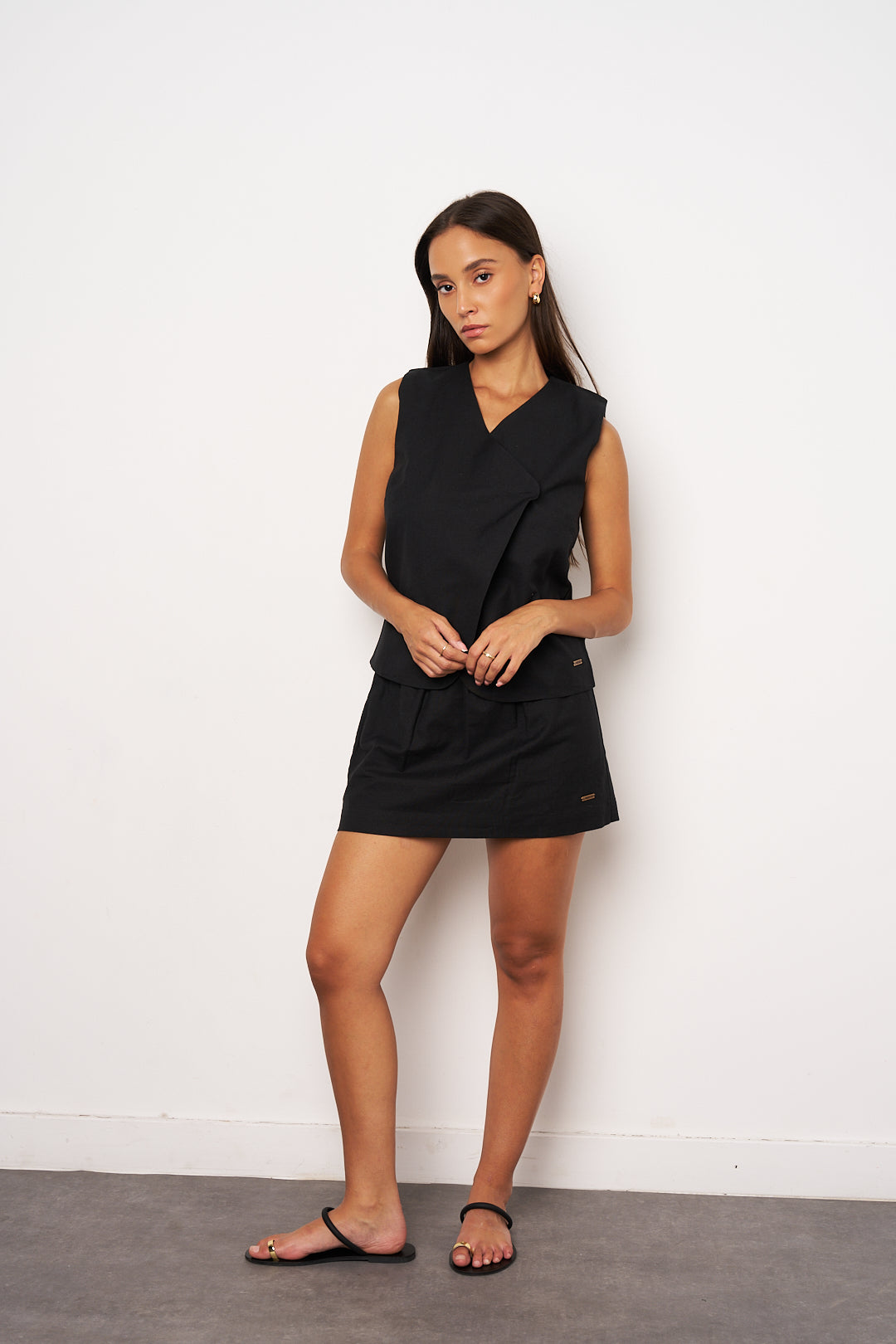 Woman wearing a black sleeveless dress against a white wall