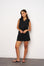 Woman wearing a black sleeveless dress against a white wall