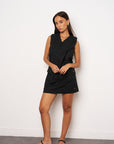 Woman wearing a black sleeveless dress against a white wall