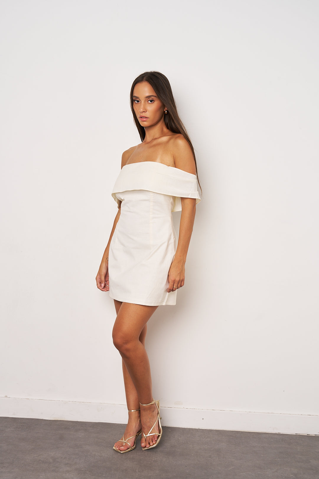 Woman wearing a white off-shoulder dress against a plain background