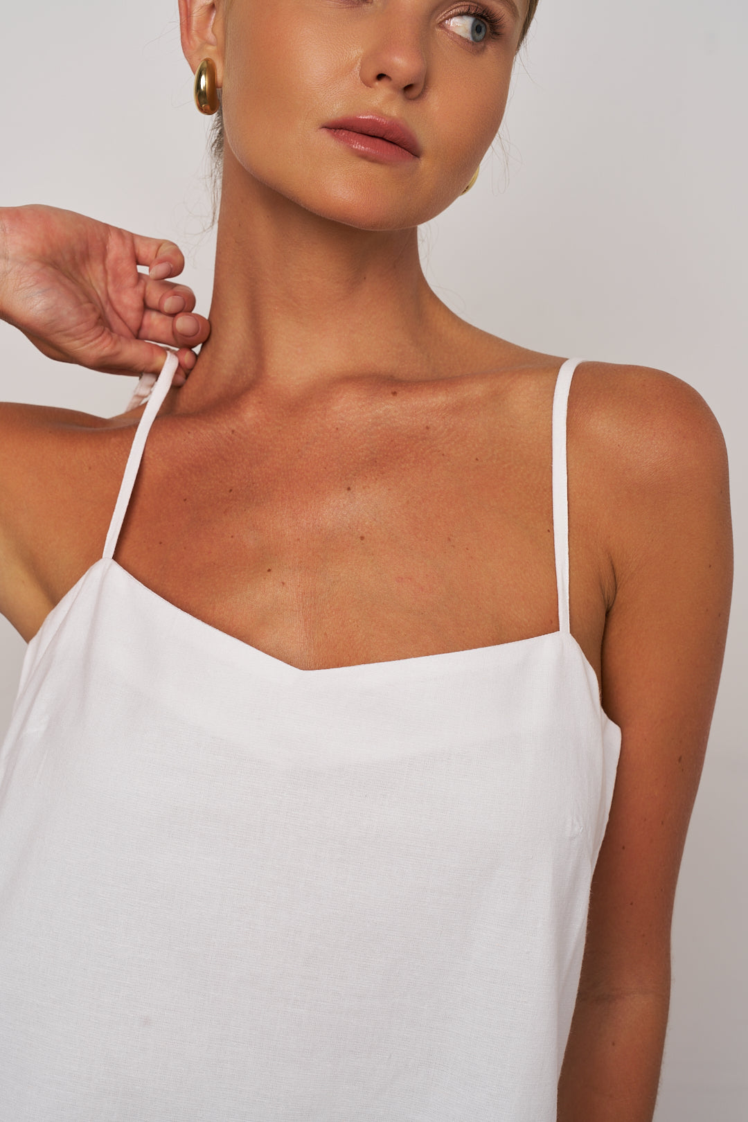Woman wearing a white slip dress with thin straps against a plain background