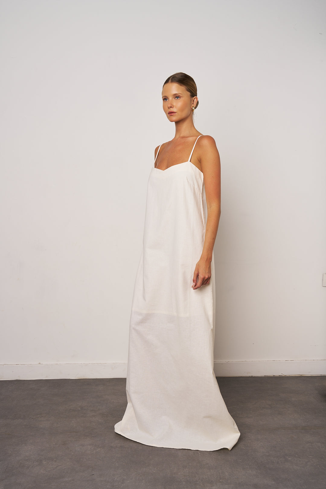 Woman wearing a white slip dress against a plain background