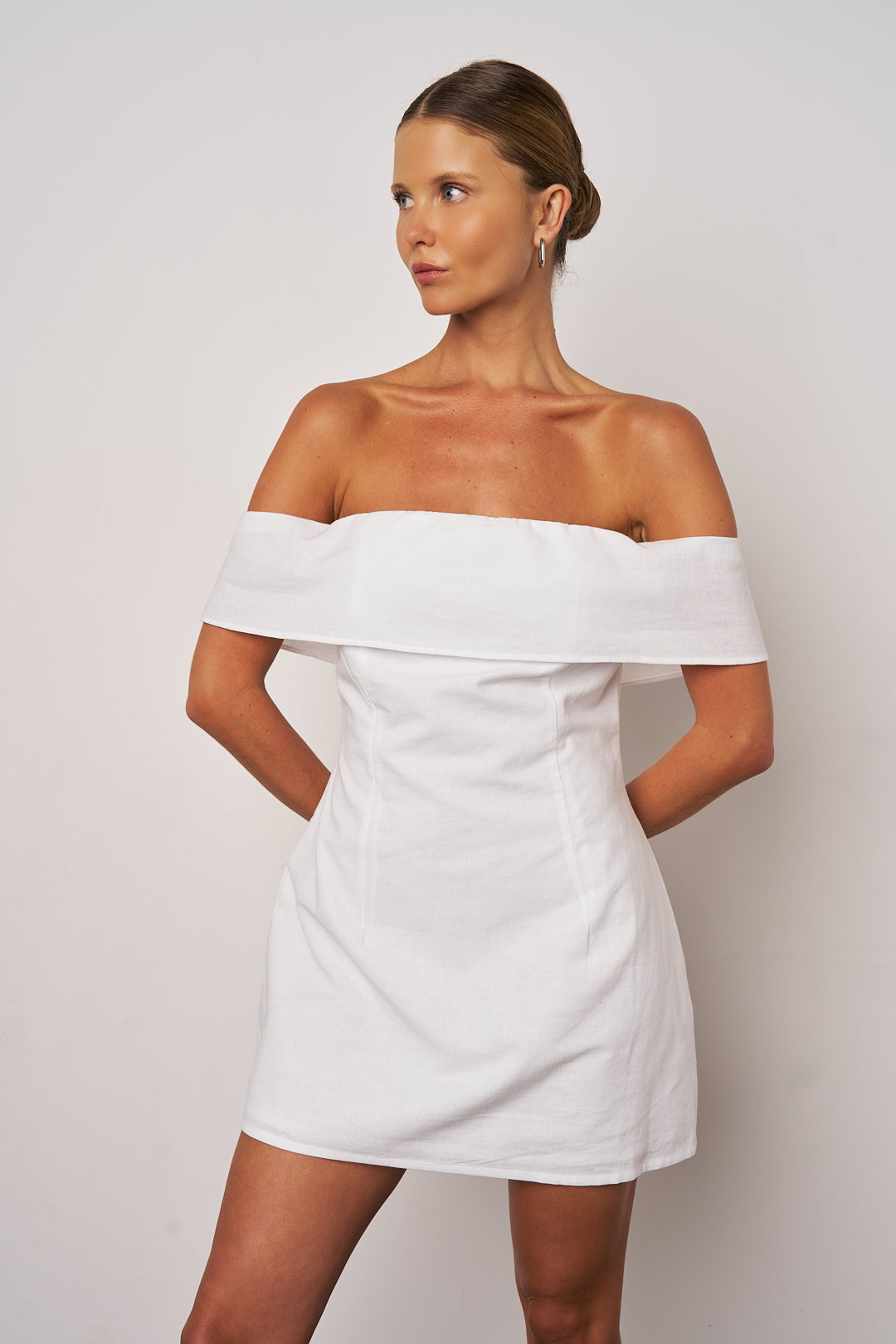 Woman wearing a white off-shoulder dress against a plain background
