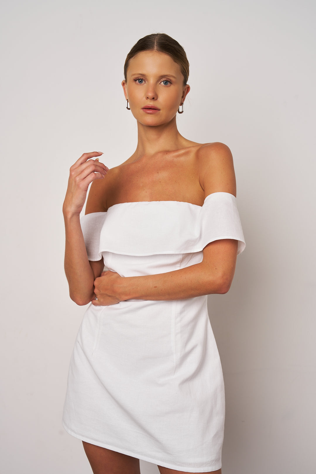 Woman wearing a white off-shoulder dress against a plain background